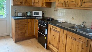 A kitchen with wooden cabinets, a stove, a microwave, and a sink. - Cottage in the Dublin Mountain (Cunard)