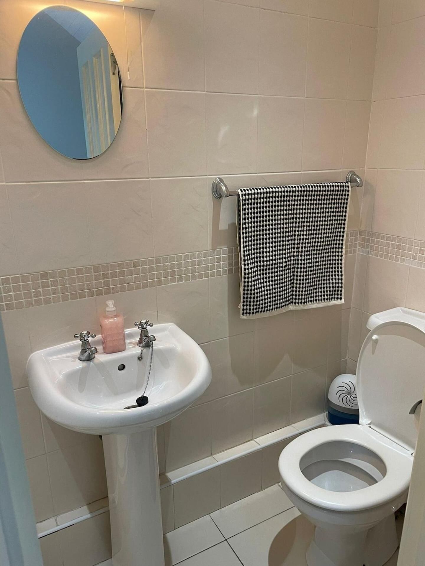 Ein Badezimmer mit einem weißen Waschbecken, einer Toilette, einem Handtuchhalter mit einem schwarz-weißen Handtuch und einem Spiegel mit blauem Rahmen.