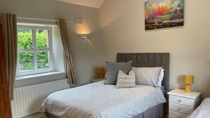 A bedroom with a large bed, two bedside tables, a window with curtains, a radiator, and a painting on the wall. - Cottage in the Dublin Mountain (Cunard)