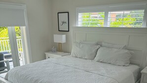 Ein weißes Bett mit gesteppter Bettdecke, ein Nachttisch mit Lampe und ein gerahmtes Bild an der Wand.