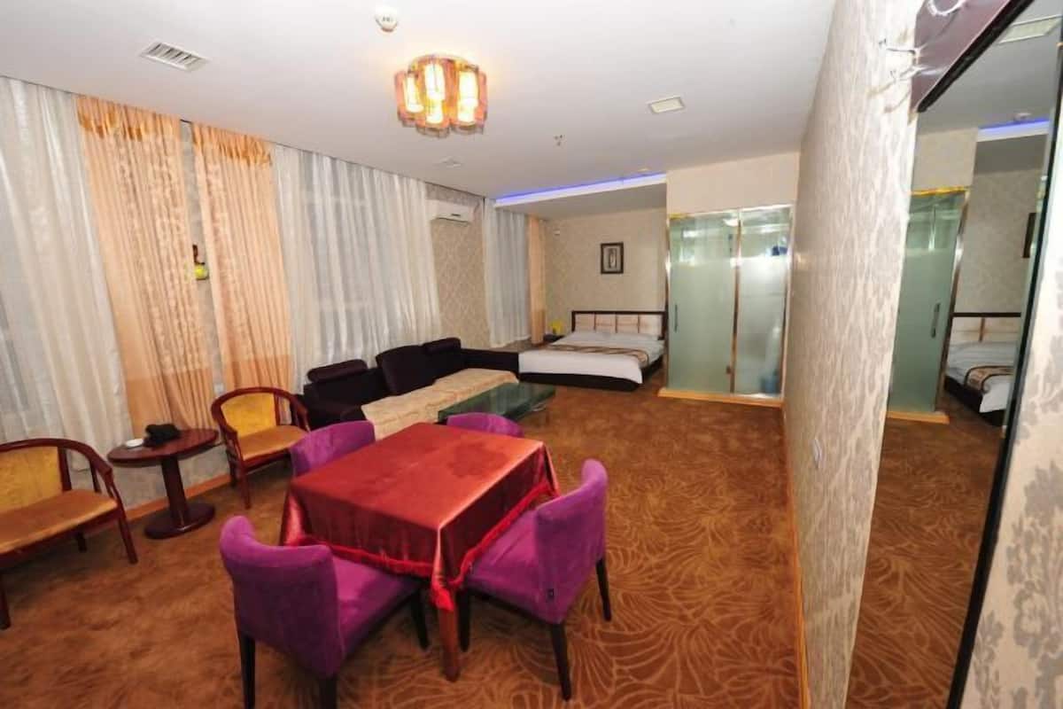 A hotel room with a sofa, a small table, and a bed. There is a mirror and a window with curtains.