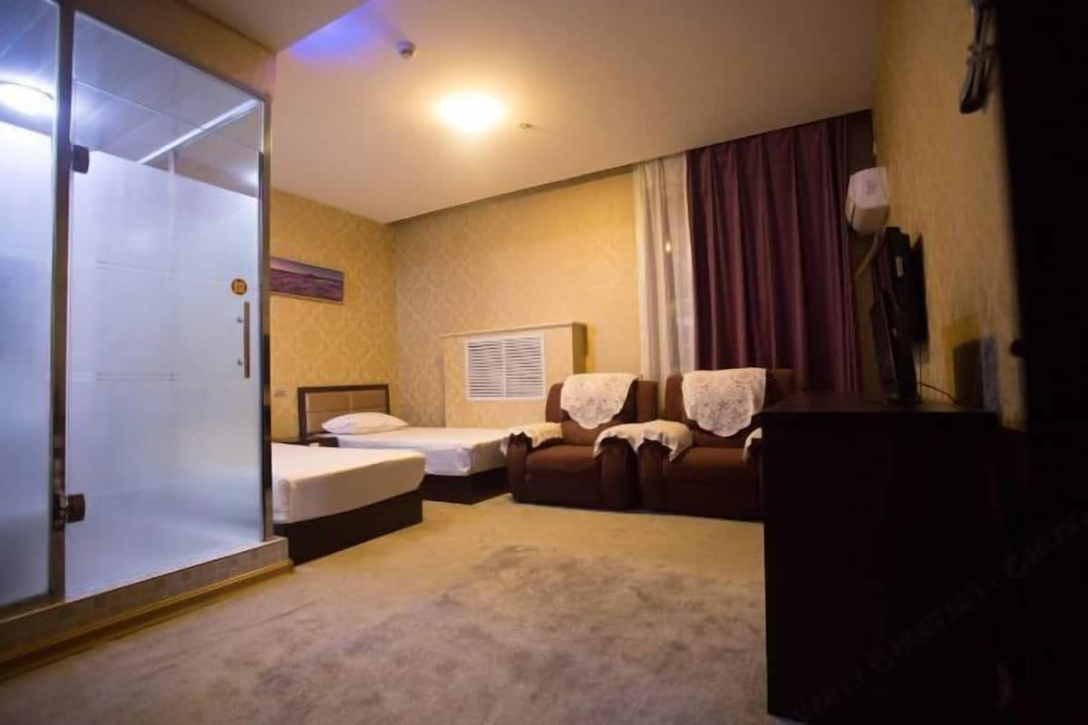 A hotel room with a bed, two chairs, a desk, a wardrobe, and a sliding door.