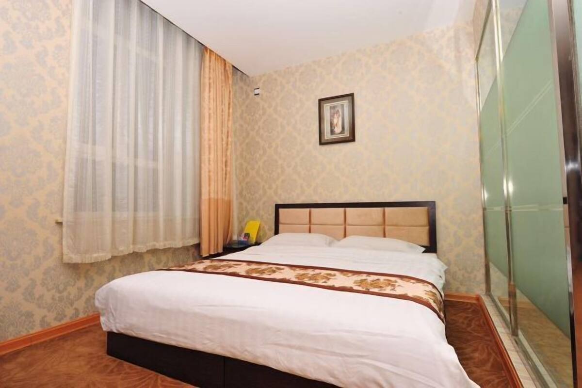 A hotel room with a bed, a nightstand, a framed picture on the wall, and a window with curtains.