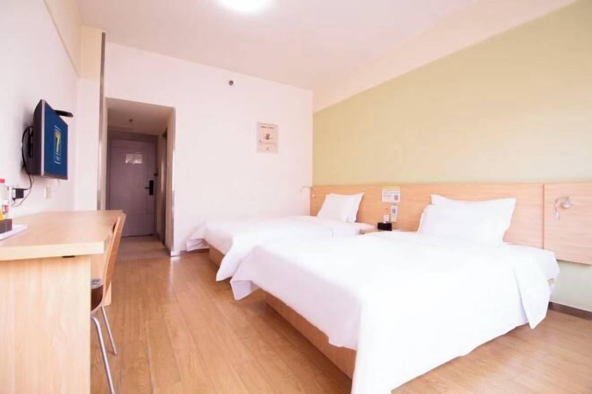 A hotel room with two beds, a desk, a TV, and a door leading to another room.