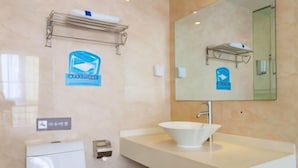 Un bany modern amb un lavabo blanc, un mirall gran i un vàter. Hi ha un dispensador de tovalloles i un paperer.