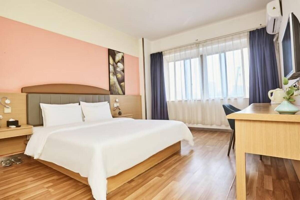 A hotel room with a bed, a desk, a chair, a nightstand, and a window with curtains.