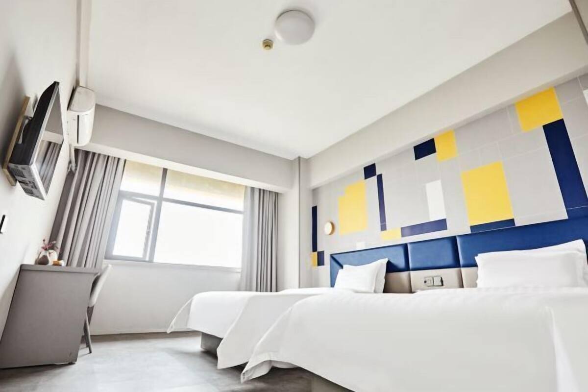 A hotel room with two beds, a desk, a TV, and a large window.