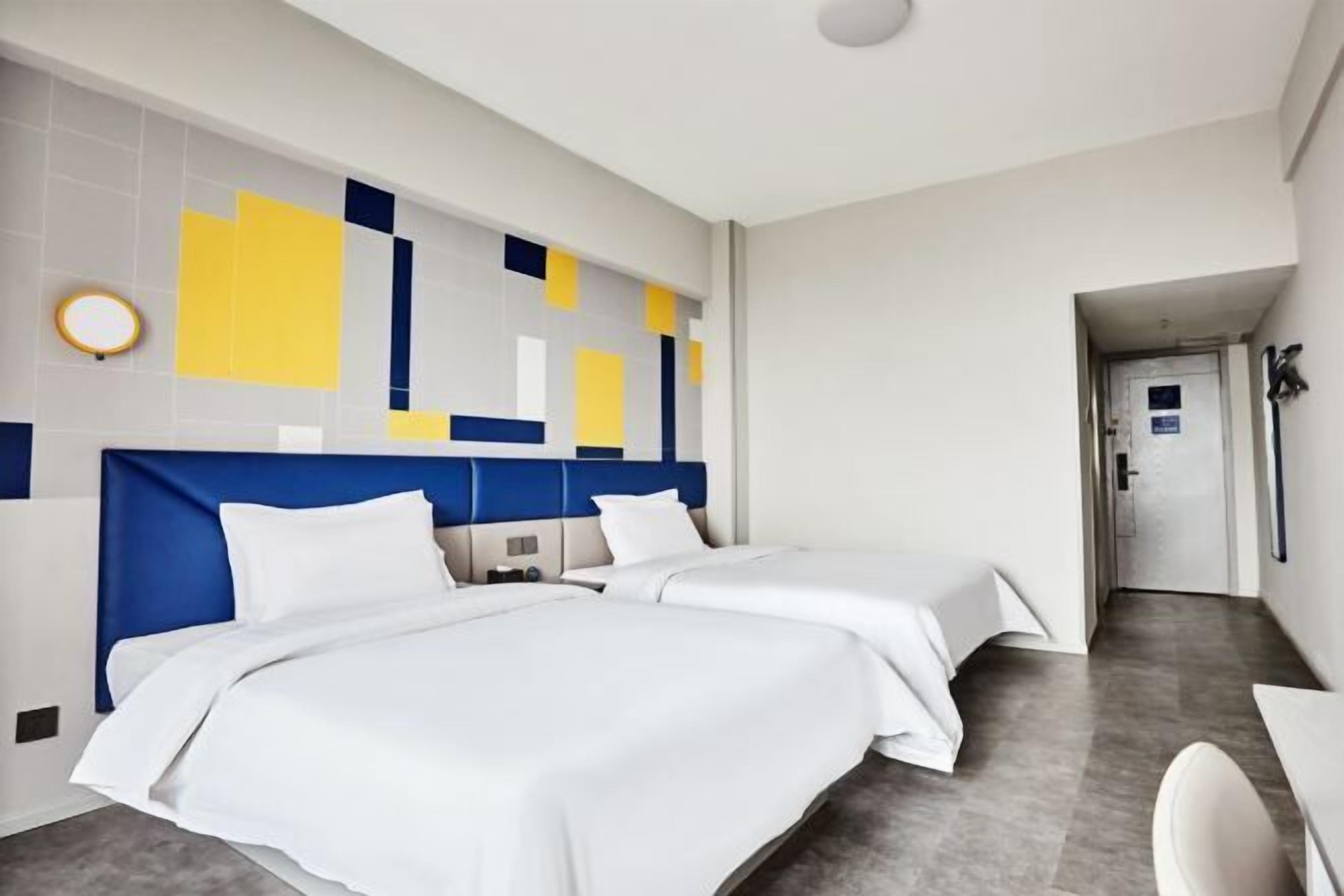 Een hotelkamer met twee bedden, een modern hoofdbord, een klein nachtkastje en een ronde wandlamp.