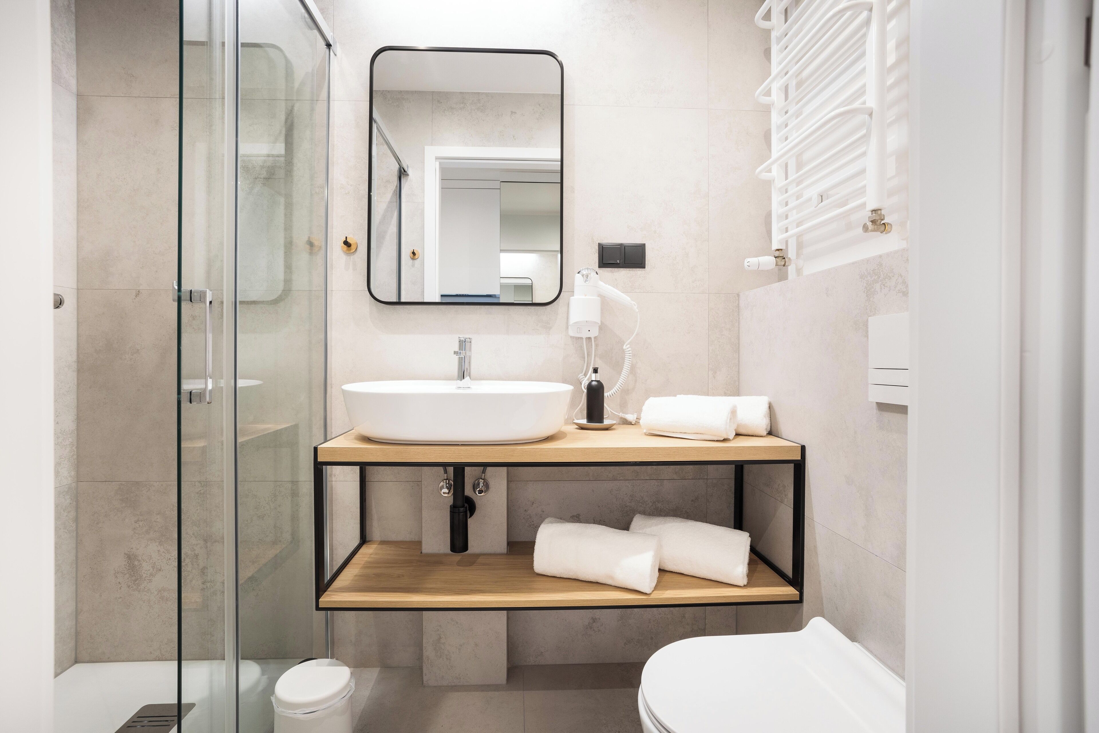 A modern bathroom with a glass shower enclosure, a white sink, a mirror, and a towel rack.