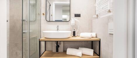 A modern bathroom with a glass shower enclosure, a white sink, a mirror, and a towel rack.