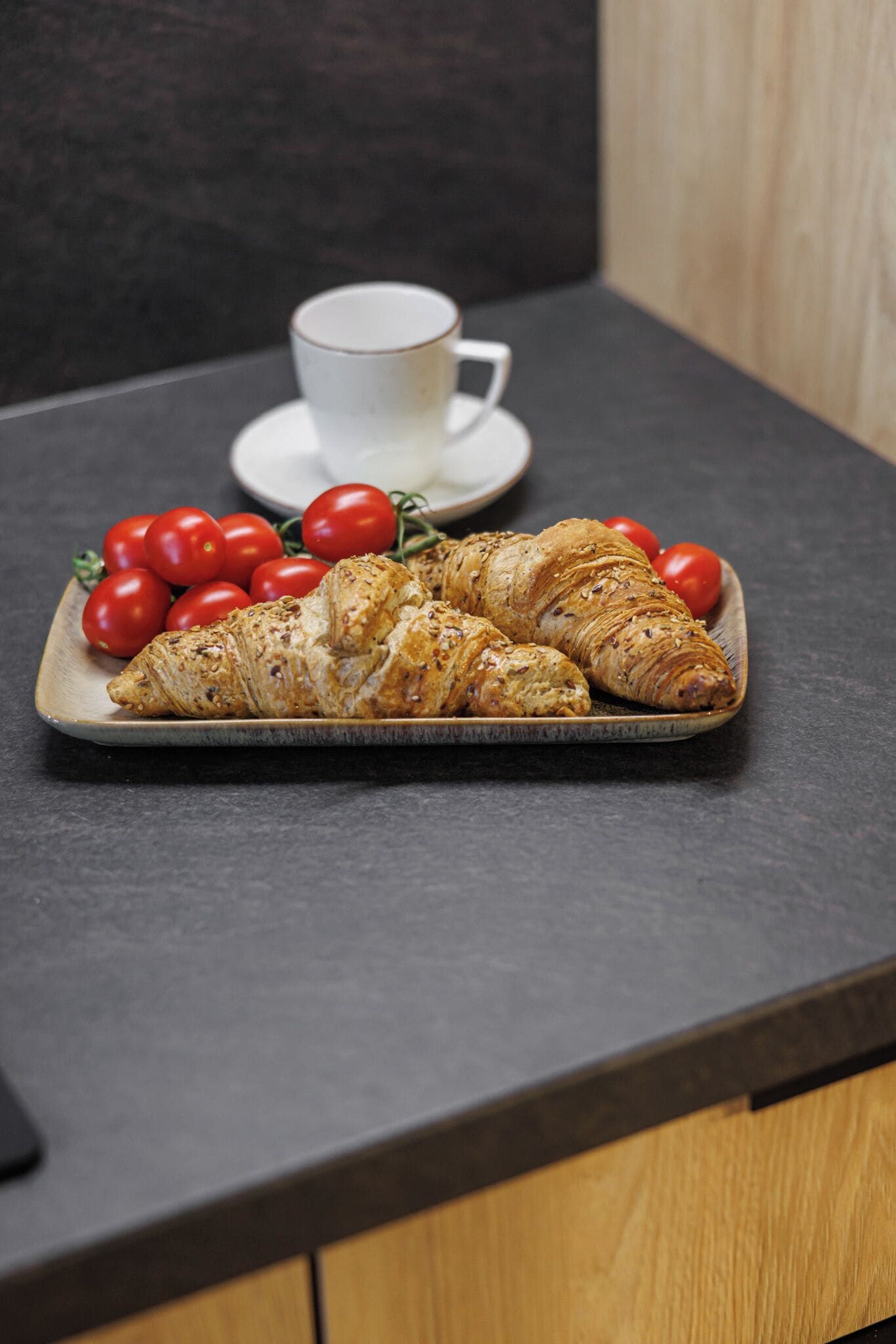 Een dienblad met croissants en kersjes op een donker aanrecht.