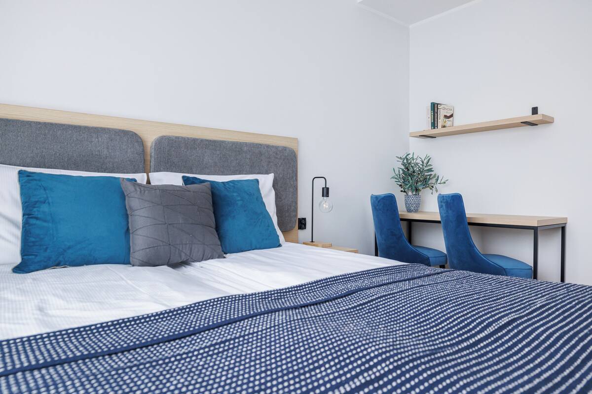 Un dormitorio moderno con una cama grande, una mesita de noche, una silla y un escritorio pequeño con un estante superior.