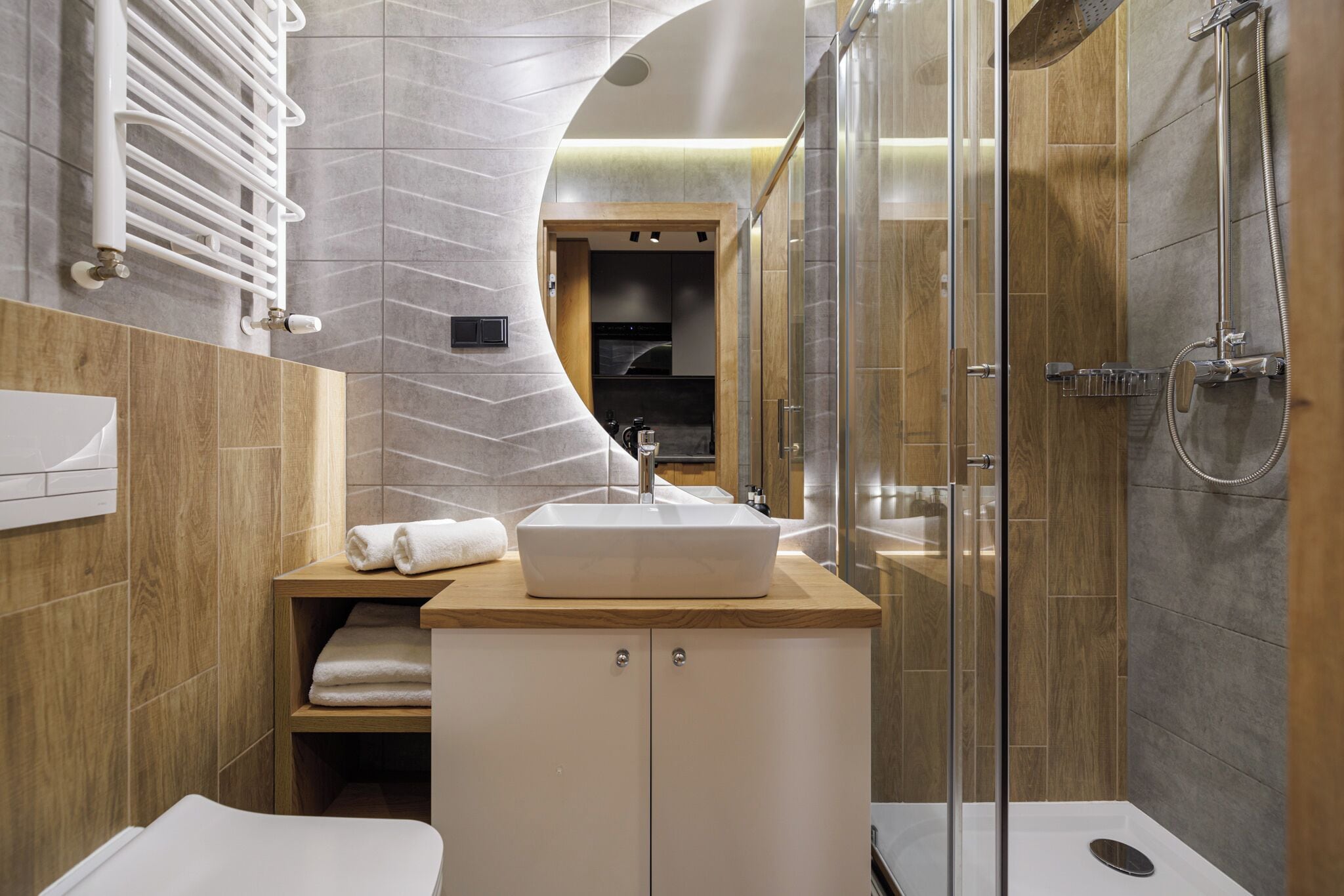 Un baño moderno con ducha envuelta en vidrio, tocador de madera con lavamanos y un perchero para toallas.