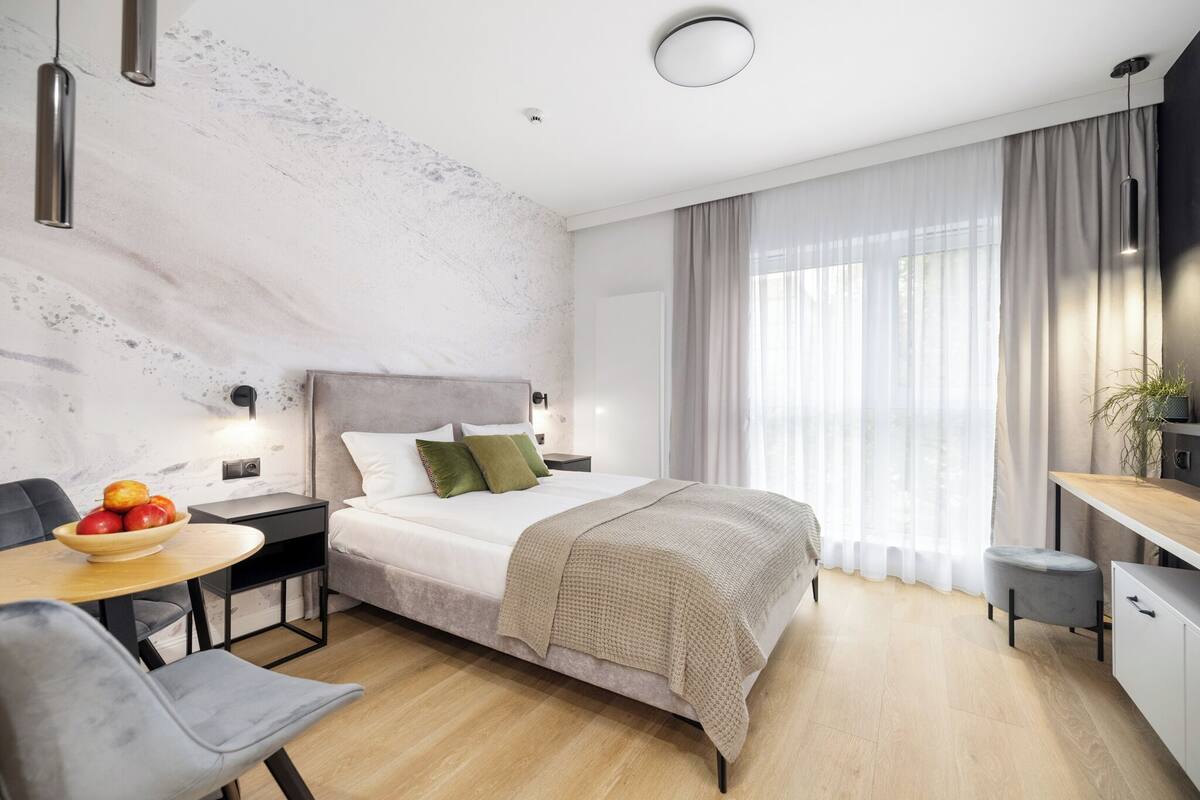 Un dormitorio moderno con cama, mesita de noche y un pequeño rincón de escritorio.