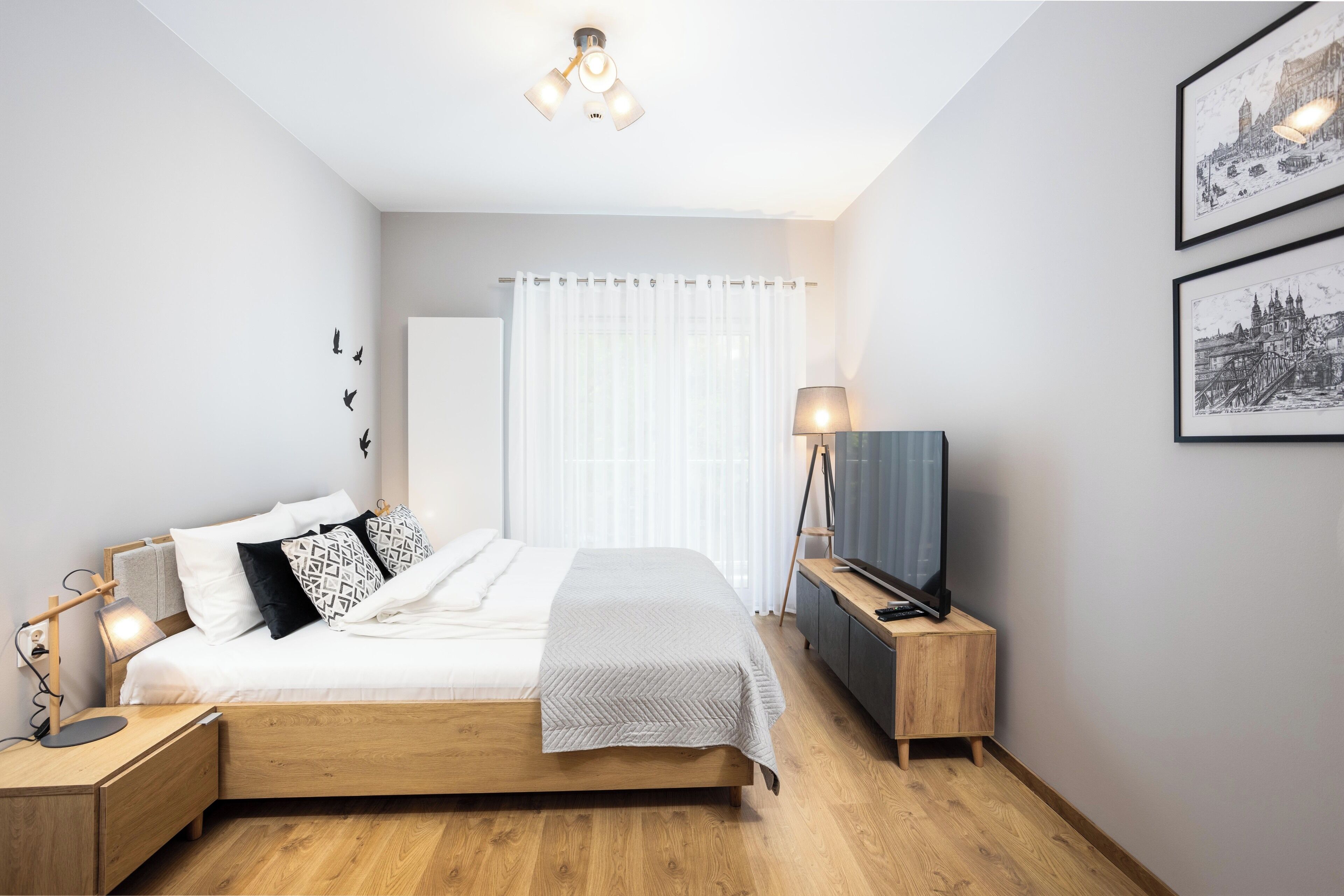 Quarto moderno com cama de madeira, mesas de cabeceira, televisão e quadros nas paredes.