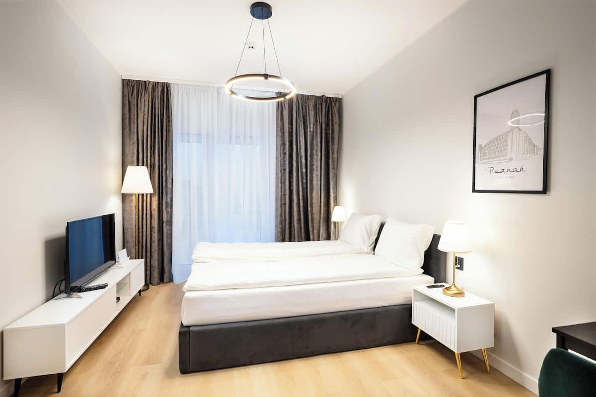 Una habitación de hotel moderna con una cama grande, un televisor de pantalla plana, mesitas de noche y un cuadro enmarcado en la pared.