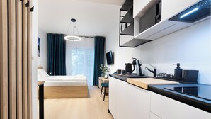 Moderni hotellihuone, jossa on sänky, työpöytä, pieni keittiö ja seinälle asennettu televisio.