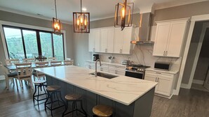 A spacious kitchen with a large island, bar stools, and modern pendant lighting. - Brand new luxury craftsman. 5000 sqft with 5 bedrooms, 5 baths and bunk room. (Six Mile)