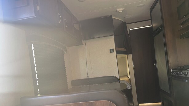 Ein kompaktes Wohnmobil-Interieur mit einer Küchenzeile, einer kleinen Sitzecke und einem schmalen Gang.