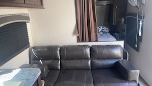 Ein gemütlicher Wohnbereich mit Ledersofa, kleinem Tisch, Fernseher und Ventilator.
