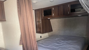 Ein kompaktes Wohnmobil-Interieur mit einer Etagenliege, Holzschränken und einer kleinen Sitzecke.