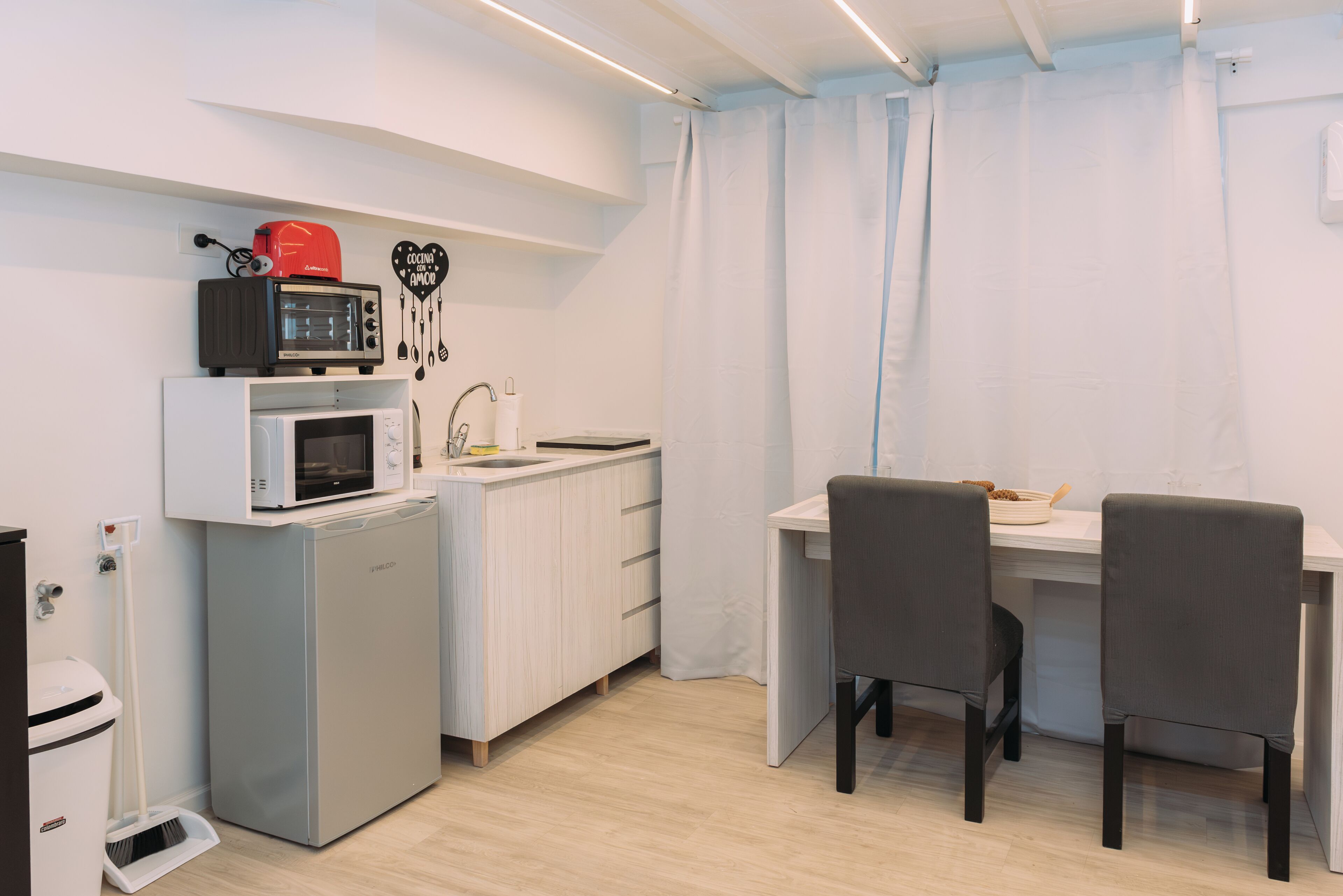 Une cuisine compacte équipée d’un four à micro-ondes, d’un grille-pain et d’un évier. Elle comprend deux chaises et une petite table à manger.