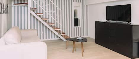 A modern living room with a staircase, a sofa, a TV, and a black cabinet.