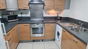 A compact kitchen with a microwave, oven, and washing machine. - Stratford Luxury Apartments (London)