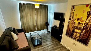 A modern living room with a sofa, a coffee table, a TV, and a painting on the wall. - Stratford Luxury Apartments (London)