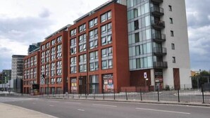 A modern multi-story building with a red facade and large windows. - Stratford Luxury Apartments (London)