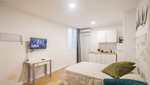 A compact room with a bed, a desk, a television, a kitchenette, and a window.