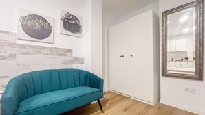 A room with a teal sofa, a white wardrobe, and two wall-mounted artworks.