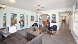 Ein großzügiger Wohnbereich mit grauem Sofa, zwei schwarzen Sesseln, einem Holztisch und einer Chandelier.
