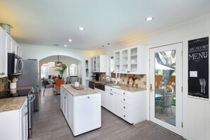 A modern kitchen with white cabinetry, a central island, and a dining area with orange chairs.