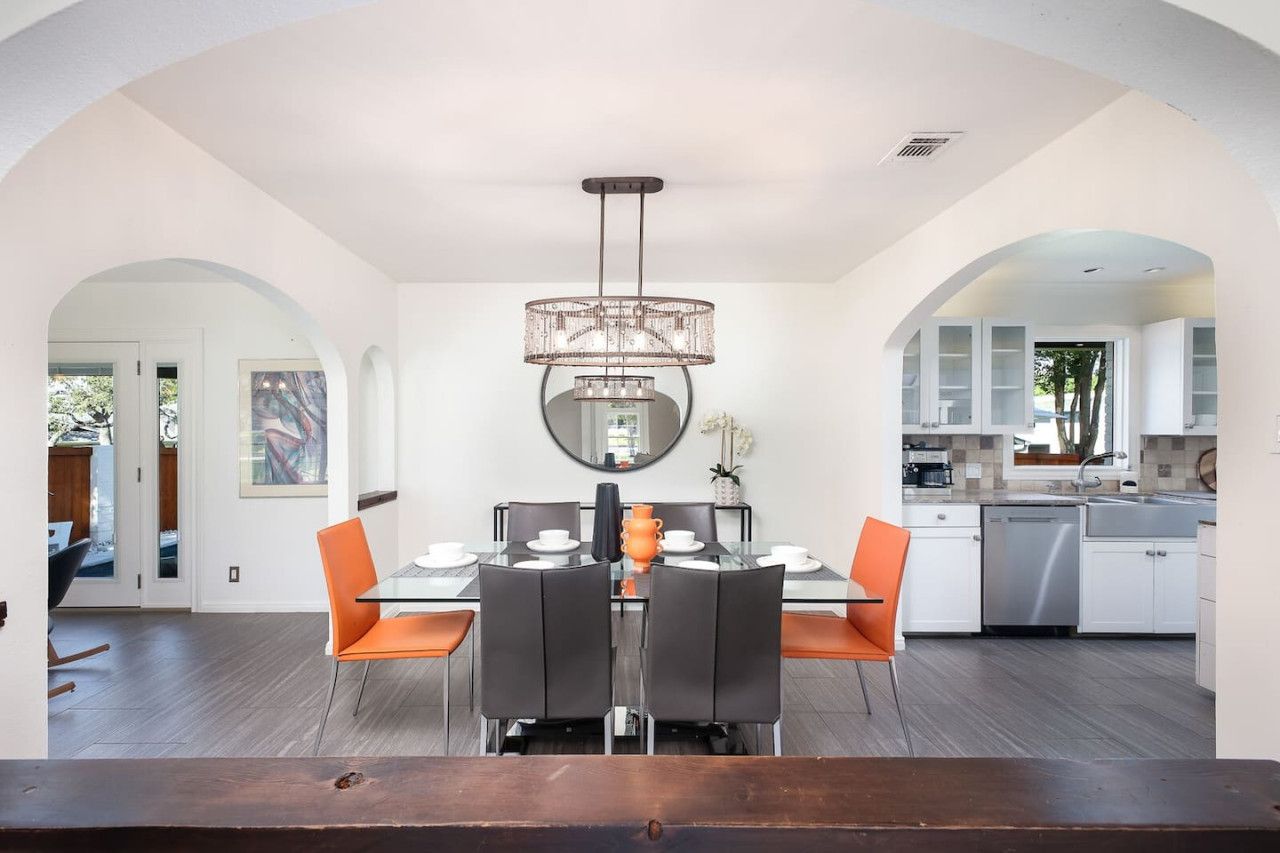 A modern dining area with a chandelier, a dining table set for four, and a kitchen in the background.