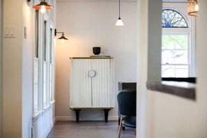 A hallway with a radiator, pendant lights, and a window with a stained glass design.