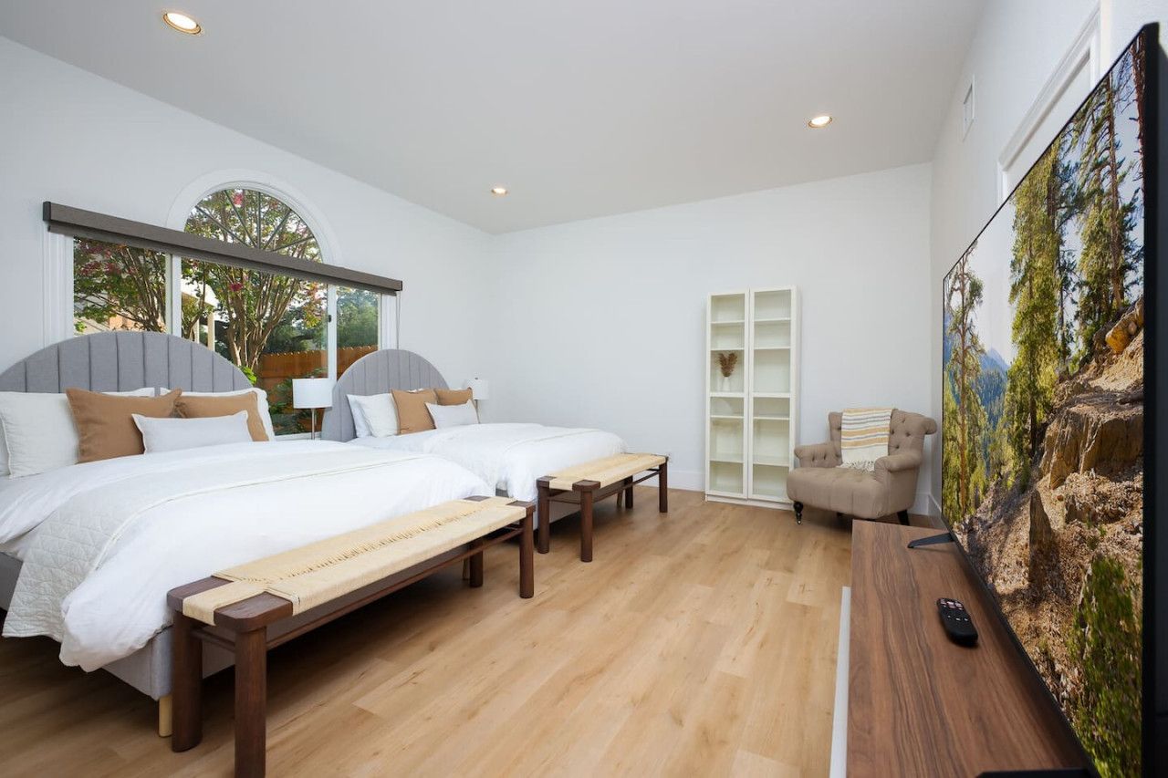 A bedroom with two beds, a TV, and a large window.