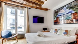 A hotel room with a bed, a chair, a TV, and a window with curtains.