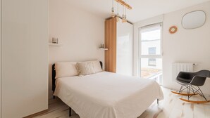A bedroom with a bed, a wooden headboard, a window, a radiator, and a black rocking chair.