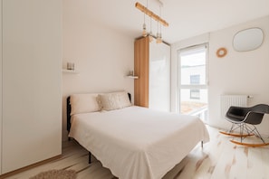A bedroom with a bed, a wooden headboard, a window, a radiator, and a black rocking chair.