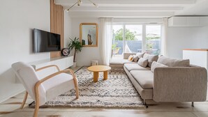 A modern living room with a sofa, chairs, a TV, and a large window.