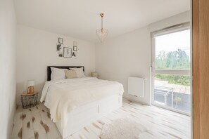 Une chambre à coucher comprenant un lit, une table de chevet, une lampe, un radiateur et une fenêtre donnant sur un paysage verdoyant.