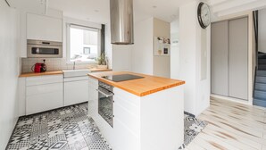 A modern kitchen with white cabinetry, a stainless steel range hood, a wooden countertop, and patterned floor tiles.