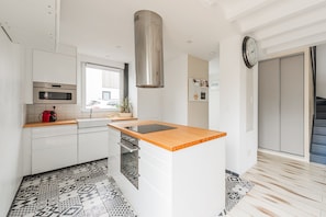 A modern kitchen with white cabinetry, a stainless steel range hood, a wooden countertop, and patterned floor tiles.