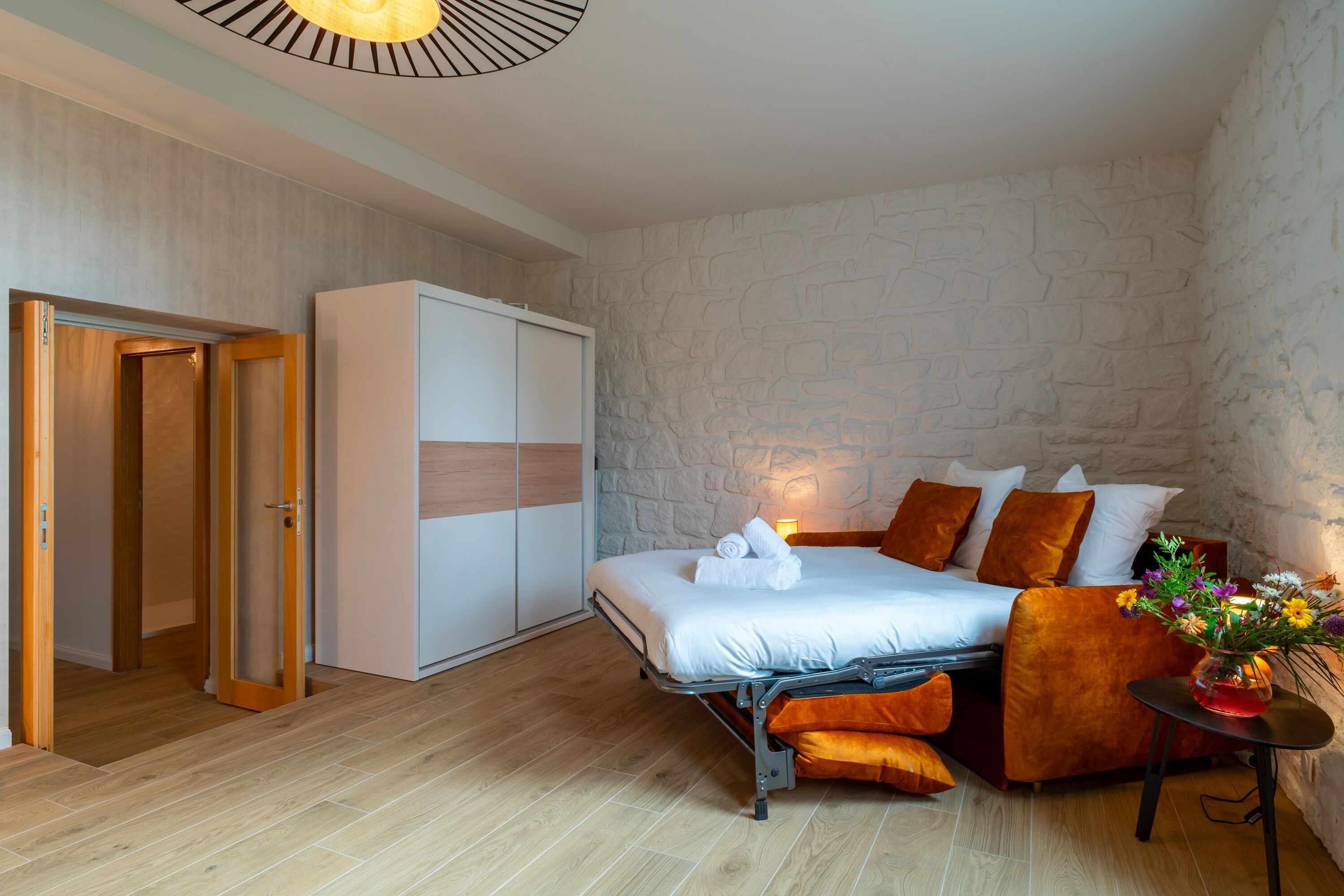 Une chambre à coucher comprenant un lit, une armoire, une petite table avec un vase et un mur orné d’un motif en pierre.