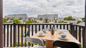 Un balcon avec une table dressée pour le dîner, donnant sur un quartier résidentiel avec des maisons et une rue.