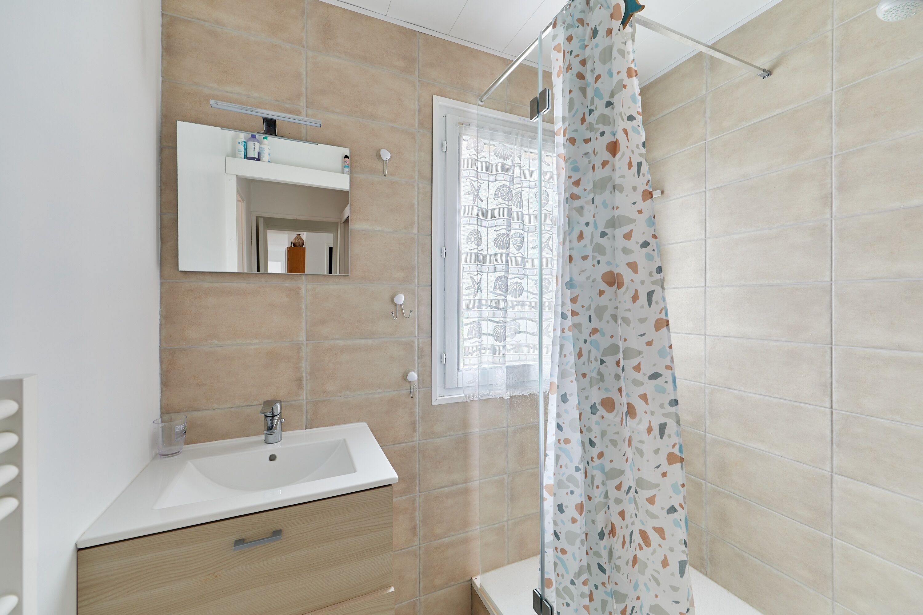 Ein Badezimmer mit Waschbecken, Spiegel, Fenster und Duschvorhang.