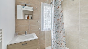 Une salle de bain avec un lavabo blanc, un miroir, une fenêtre et un rideau de douche.