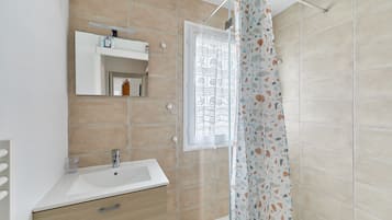 Une salle de bain avec un lavabo blanc, un miroir, une fenêtre et un rideau de douche.