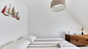 Une chambre à coucher comprenant un lit, une commode en bois, un luminaire suspendu et une œuvre d’art murale.